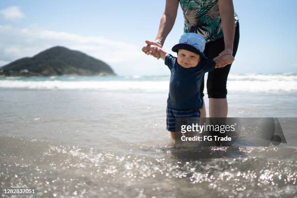 Baby boy being held by the hand while entering the sea at the beach