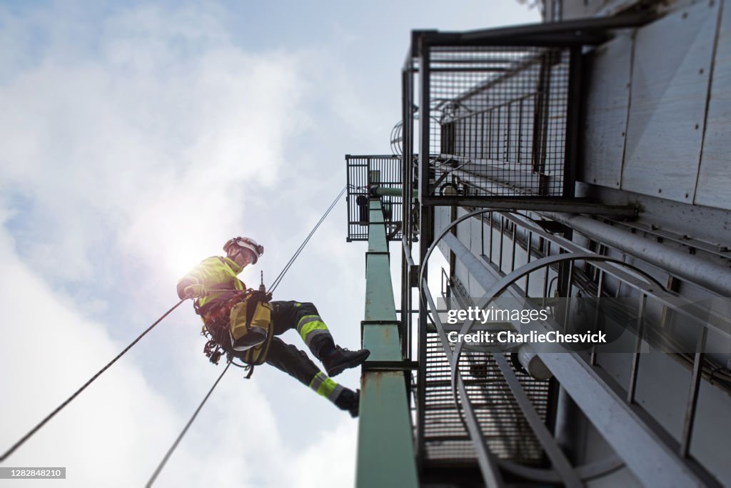 Epic view on Manual rope access technician - worker abseil from tower - antenna in sun beams