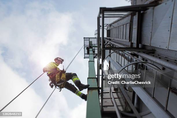 epic view on manual rope access technician - worker abseil from tower - antenna in sun beams - safety harness stock pictures, royalty-free photos & images