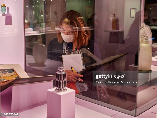 Visiting journalist wears a protective mask while watching glass objects on display at the "René Lalique e a Idade do Vidro, Arte e Indústria" during...