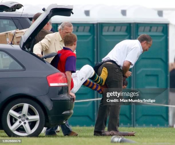 Prince Harry sits in the boot of his Audi car whilst his police protection officer removes his polo boots after playing in a charity polo match the...