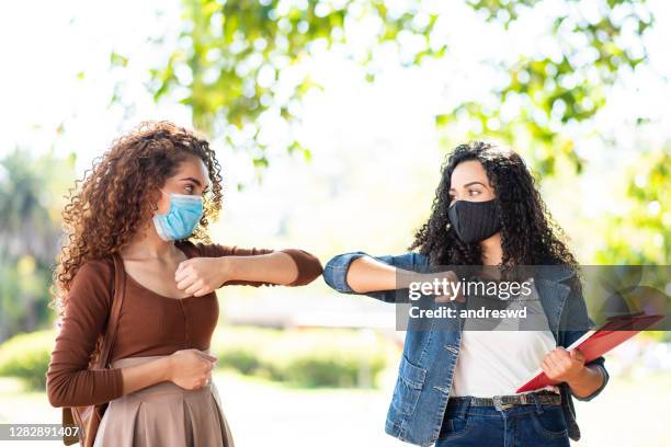 dois jovens se encontrando no campus da universidade. de volta à escola durante a pandemia e aperto de mão com o cotovelo - máscara cirúrgica - fotografias e filmes do acervo