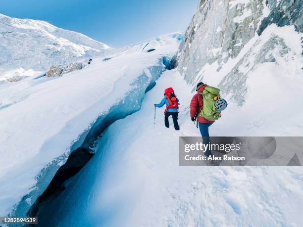 two mountain climbers through deep snow in gully with pure, blue ice on one side - whistler winter stock-fotos und bilder