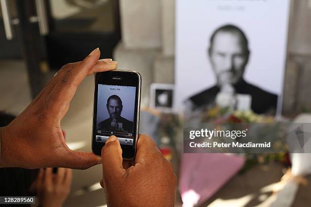 Man uses an iphone to photograph tributes to Apple Computer co-founder Steve Jobs outside The Apple Store in Covent Garden on October 6, 2011 in...