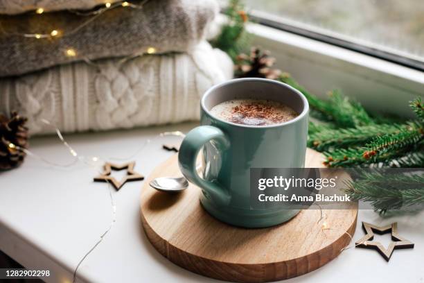 cozy home picture of blue ceramic cup with coffee on window sill, christmas decorations, warm knitted sweaters and pine tree green branches in background - hot chocolate stock pictures, royalty-free photos & images