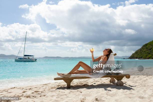 lächelnde frau toastet mit cocktail in einem teak-lounge-sessel an einem tropischen strand - margarita beach stock-fotos und bilder