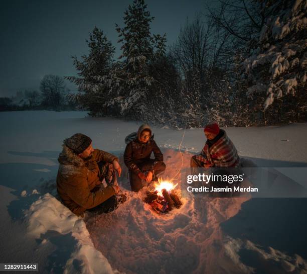 together around camping fireplace in snowy mountain forest at night - boy scout camping stock pictures, royalty-free photos & images