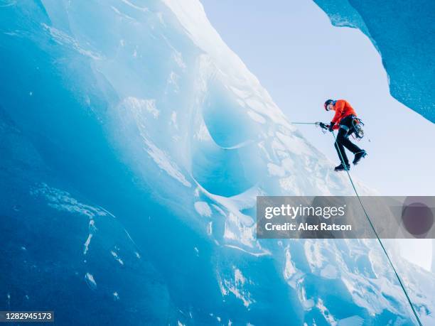 a ice climber rappels down a vertical blue ice face into a crevasse on a glacier - eisklettern stock-fotos und bilder