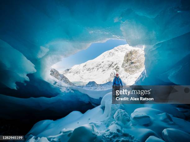 a male ice climber stands in the intrench way to a large ice cav - extremlandschaft stock-fotos und bilder