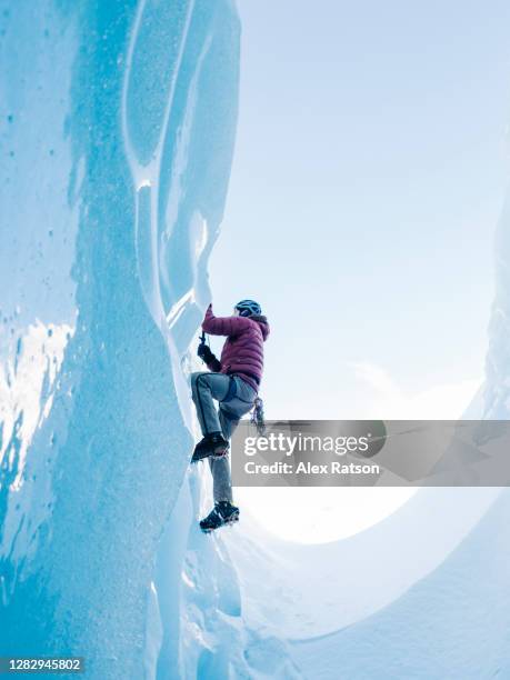 ice climber ascends dead vertical pure, blue ice face out of crevasse - eisklettern stock-fotos und bilder