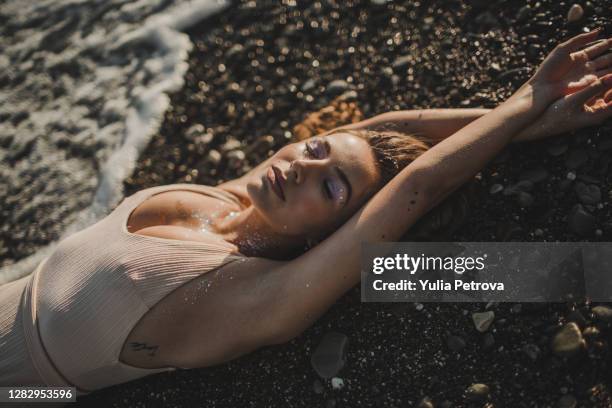 tanned sexy girl lying on the black sand on the beach - tanned body stock pictures, royalty-free photos & images