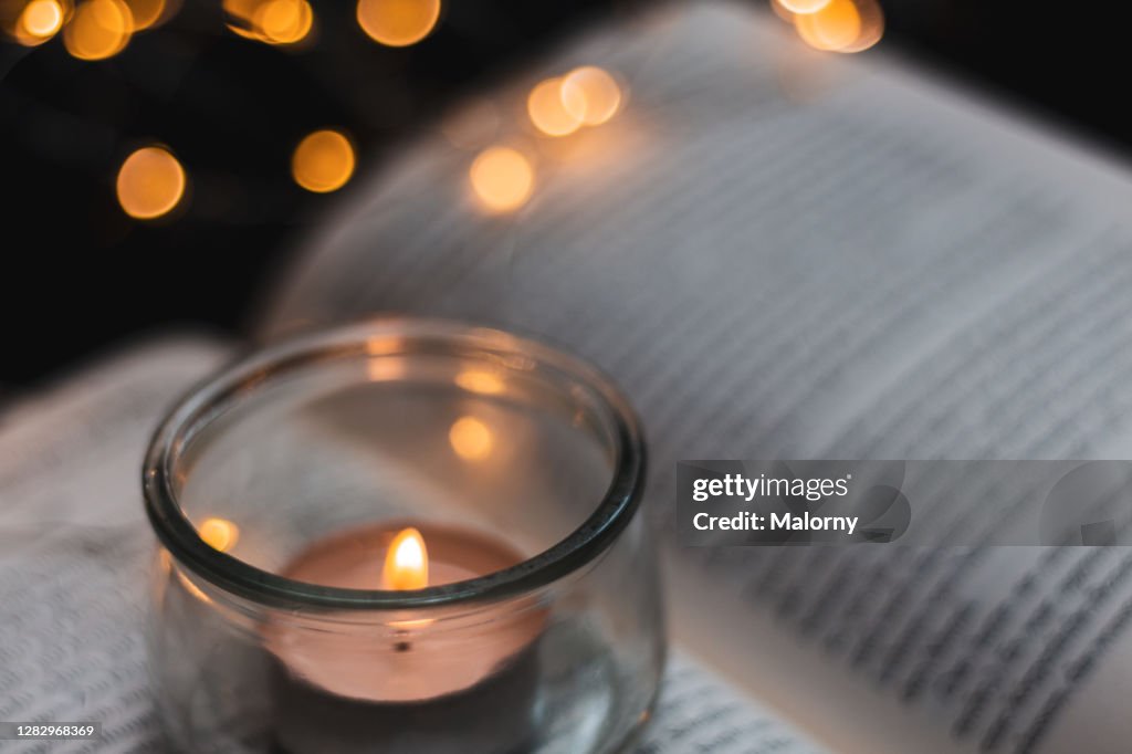 Close-up of tea light on a book with fairy lights in the back on black background.