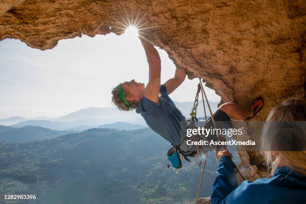 young man climbs in overhanging cave in the morning - rock overhang stock pictures, royalty-free photos & images