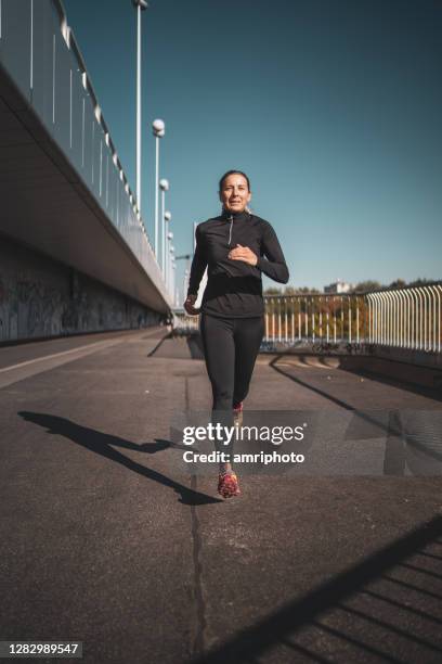 frau in schwarzem lauf tragen joggen über stadtbrücke - läufer dramatisch stock-fotos und bilder