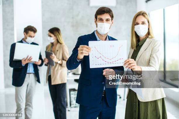 business colleague holding paper chart and looking at camera inside modern office - new business covid stock pictures, royalty-free photos & images