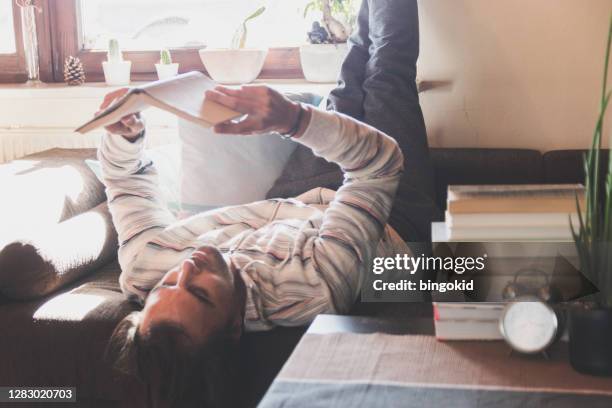 man lying on sofa reading a book - stack of sun lounges stock pictures, royalty-free photos & images