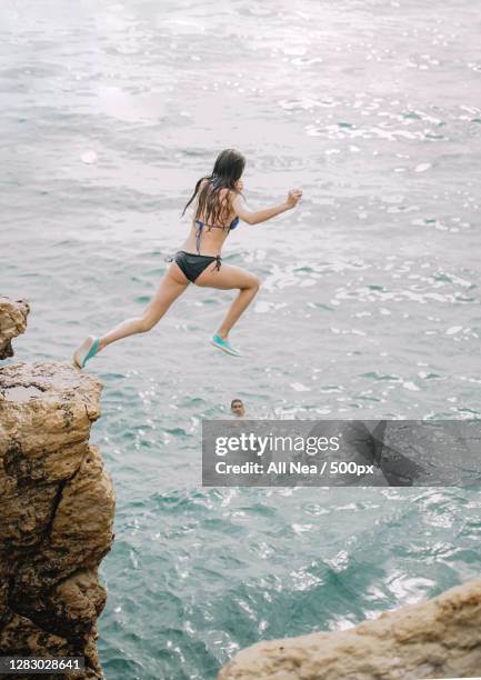 caucasian woman leaping from rock into the ocean,spain - salto desde acantilado fotografías e imágenes de stock