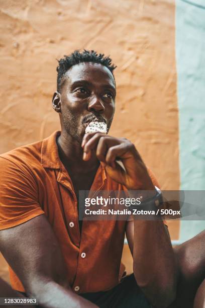 young handsome black man wears an orange shirt eats ice cream,ko pha ngan,thailand - black man eating stock pictures, royalty-free photos & images