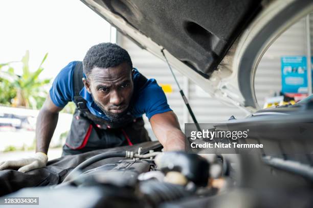 vehicle engine investigation and reconstruction service process. a car mechanic inspecting engine at auto repair center. - african american mechanic stock-fotos und bilder