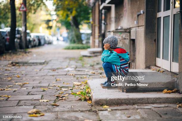 junge sitzt allein auf der straße - homeless child stock-fotos und bilder