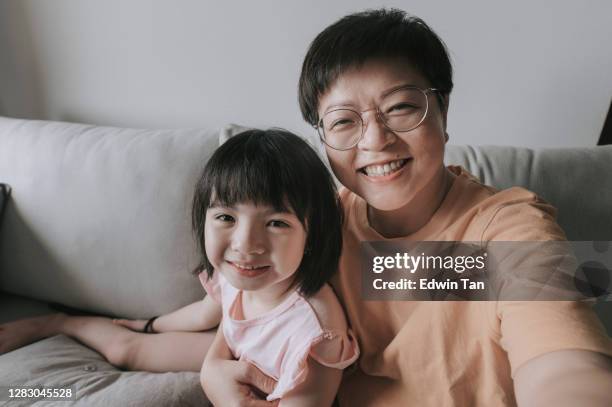 aziatische chinese jonge meisjes die aan haar vader spreken gebruikend digitale tablet online in woonkamer op bank gelukkig met haar moeder naast - mother daughter webcam stockfoto's en -beelden