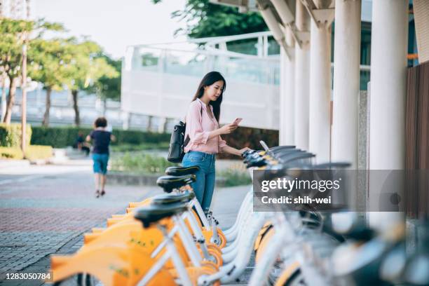 asian women renting shared bicycle in city centre - bike sharing stock pictures, royalty-free photos & images