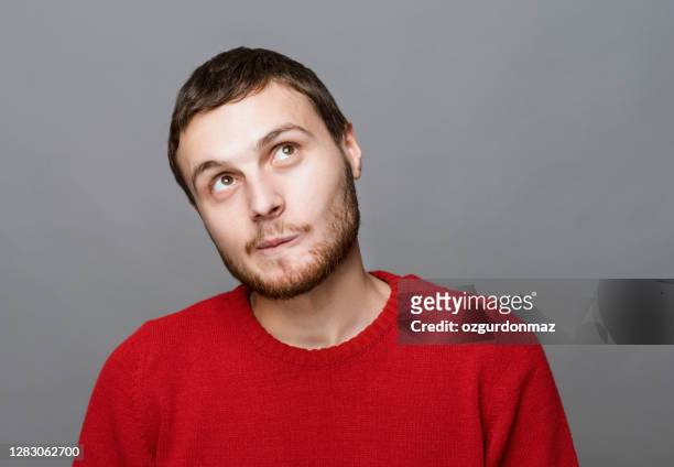 portrait shot of casual man looking up thoughtfully standing at isolated gray background - stubble imagens e fotografias de stock
