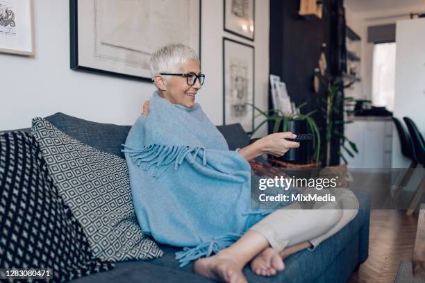 mature woman warming with blanket and watching tv at home - wrapped in a blanket stock pictures, royalty-free photos & images