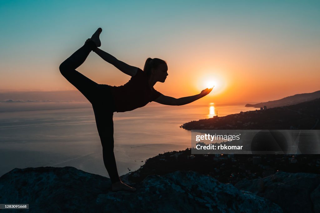 Meditation and concentration in difficult yoga pose balancing on edge of cliff against backdrop of sunset on sea coast