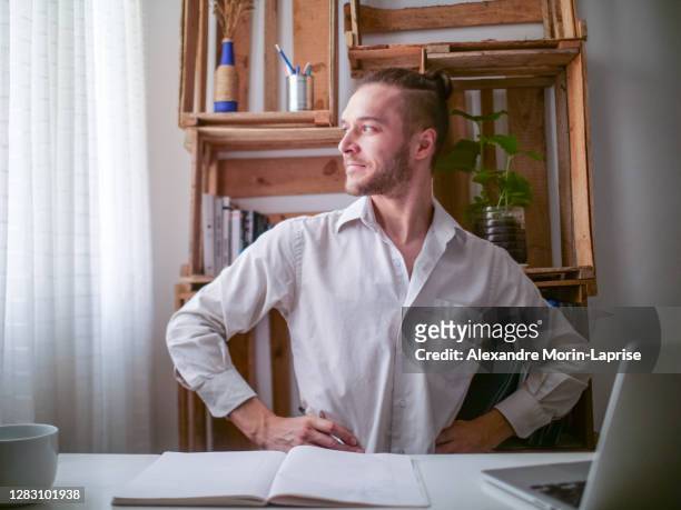 Young Caucasian Man in White Shirt Sitting at a Desk Stares at the Window Looking Proud and Satisfied