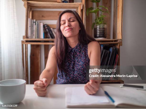 young hispanic woman at a desk is angrily clenching her fists on the table - bolivianischer abstammung stock-fotos und bilder