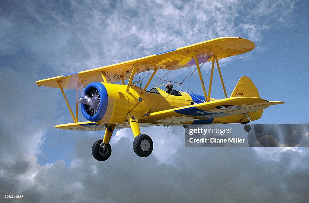 Yellow Stearman 5YP bi-plane flying in cloudy sky