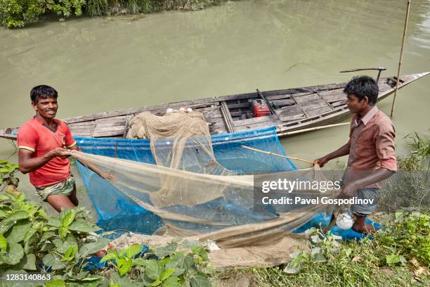 fishermen taking care of their fishing nets on the shore of kirtonkhola river in bangladesh - fisherman stock pictures, royalty-free photos & images
