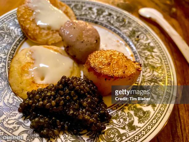 a large helping of caviar with blinis (russian mini crepes) crème fraiche ans seared sea scallops.  served on formal china with mother of pear spoon. - royalty free stock pictures, royalty-free photos & images