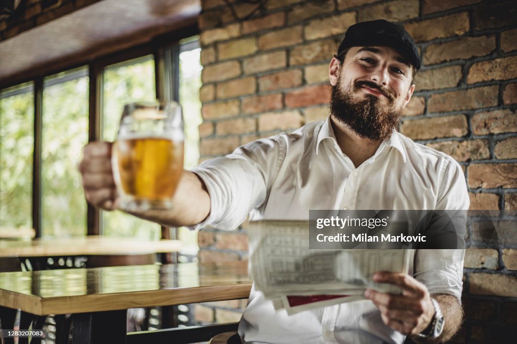 Een knappe mens zit in een Ierse staaf en drinkt bier - Bearded Hipster geniet van een bier terwijl het zitten in een staaf
