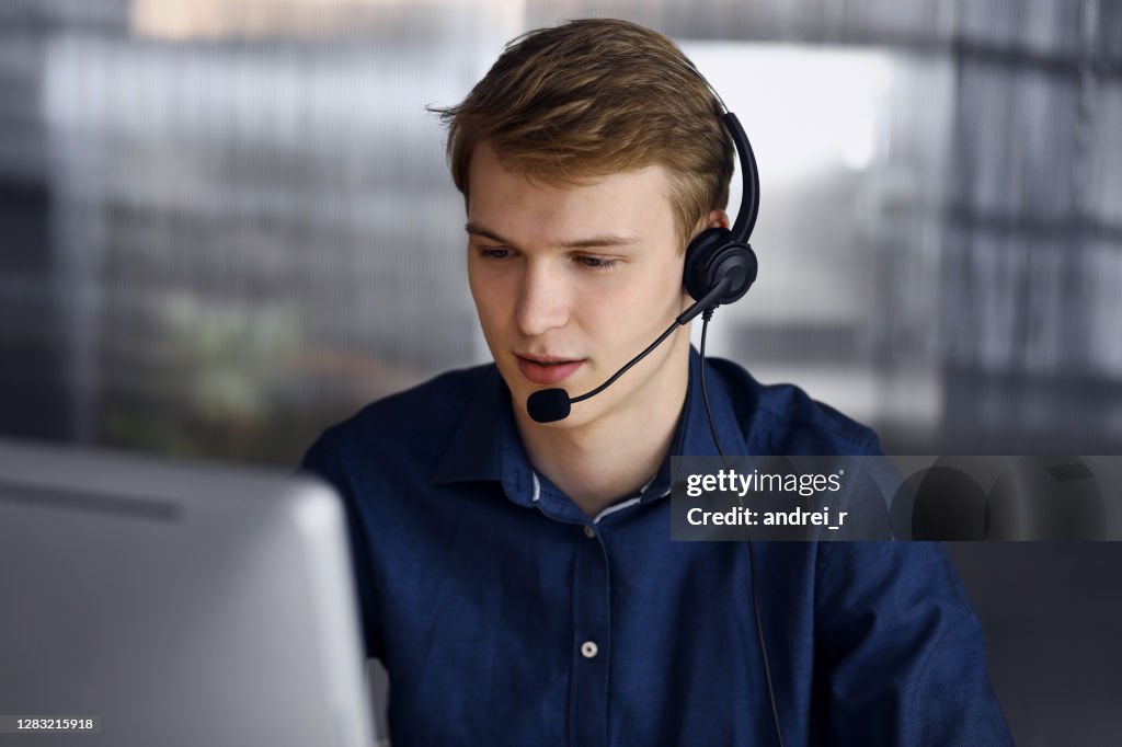Young blond businessman using headset and computer at work. Startup business means working hard and out of time for success achievement