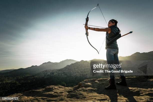 young woman taking aim with bow and arrow - hunting arrow foto e immagini stock