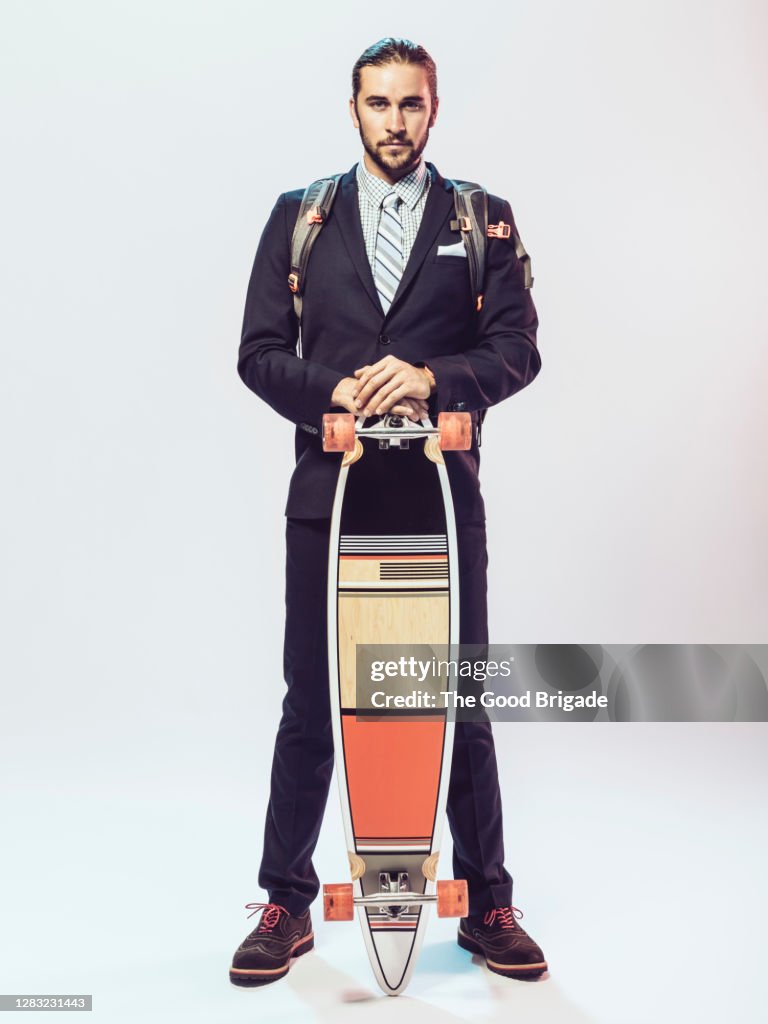 Portrait of businessman standing against white background with skateboard