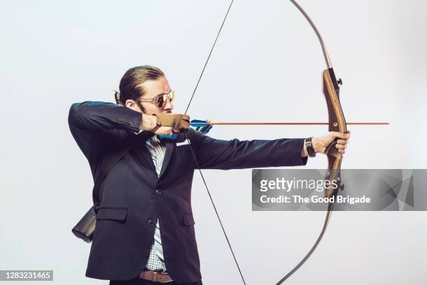 portrait of businessman aiming a bow and arrow in studio - hunting arrow stock-fotos und bilder