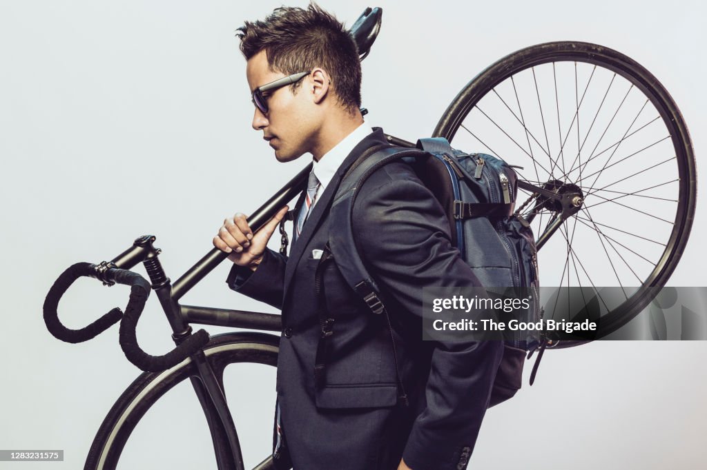 Businessman holding bicycle on shoulder against white background