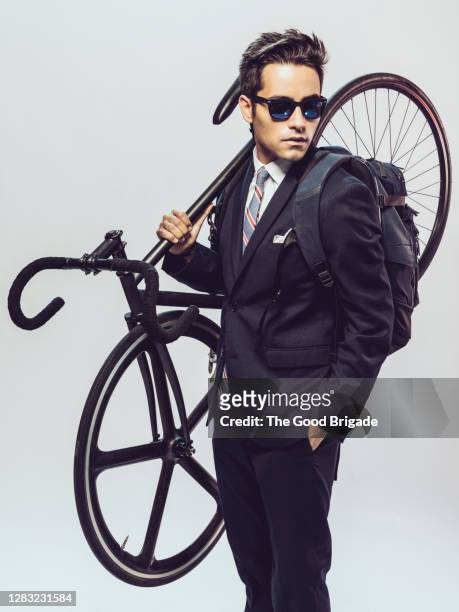 young man in suit with backpack and bike standing on white background - white suit and tie stock pictures, royalty-free photos & images