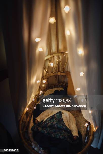 sleepy boy taking a nap inside of cozy crib with canopy and garland at home. high angle view of baby sleeping with illuminated string lights on rattan moses basket. christmas decoration around. - canopy tent stock pictures, royalty-free photos & images