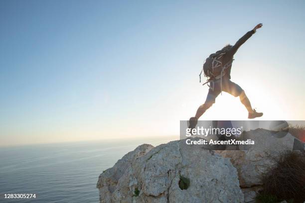 hiker jumps across mountain ridge at sunrise - leap forward stock pictures, royalty-free photos & images