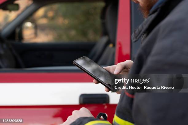 man with helmet and firefighter equipment with fire truck with mobile phone - 911 cellphone stockfoto's en -beelden