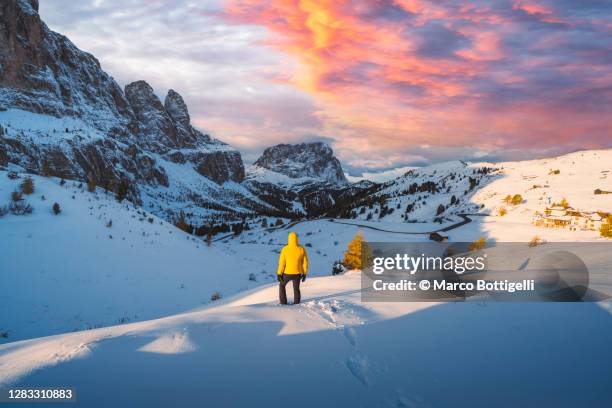 man standing in deep snow admiring sunset in the dolomites, italy - val gardena stock-fotos und bilder