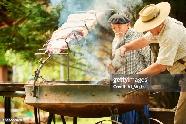 zwei ältere männer grillen gekonnt ein großes stück fleisch - asado stock-fotos und bilder