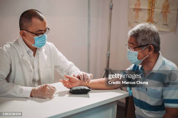 asian chinese male acupuncturists taking pulse diagnosis works for his patient at chinese medicine shop - chinese herbal medicine stock pictures, royalty-free photos & images