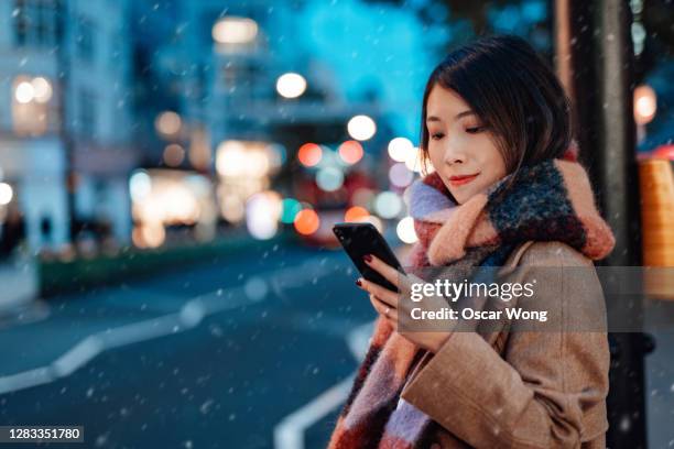 young woman using smartphone in the city at night - woman snow outside night stock pictures, royalty-free photos & images
