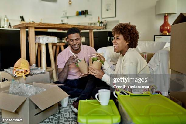young afro-caribbean couple enjoying take-out on moving day - sitting on ground stock pictures, royalty-free photos & images