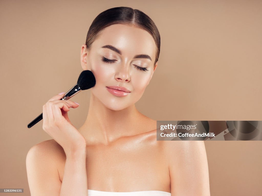 Schöne junge Frau, die Foundation Powder aufträgt